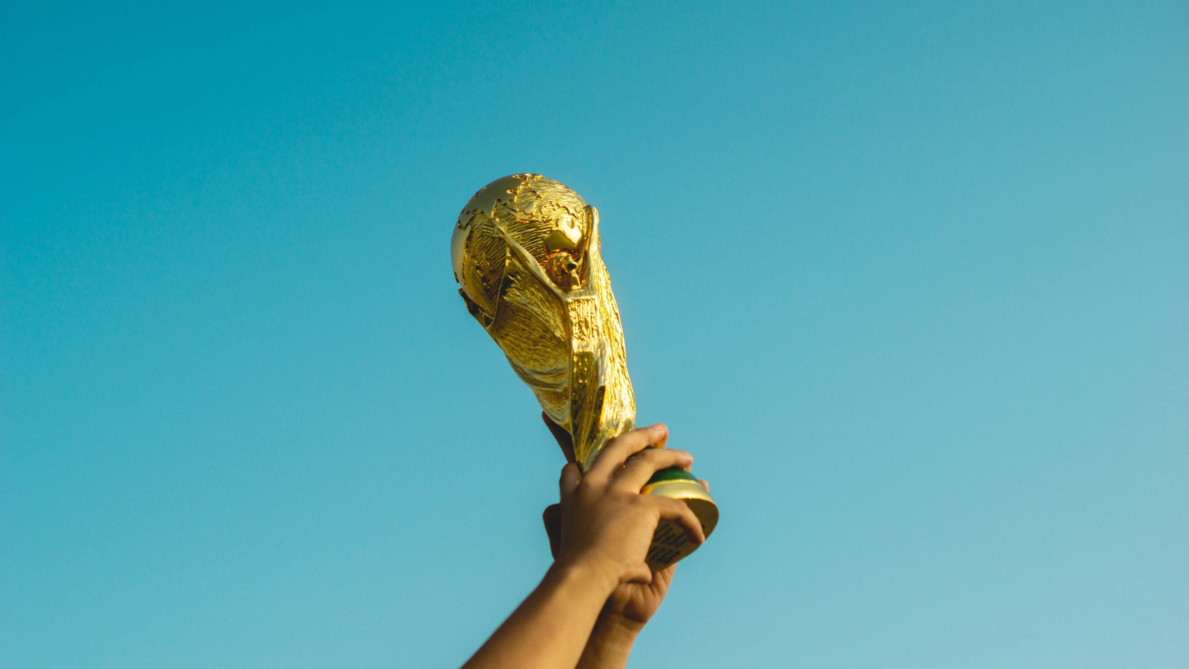 World Cup Trophy being held against a clear blue sky.